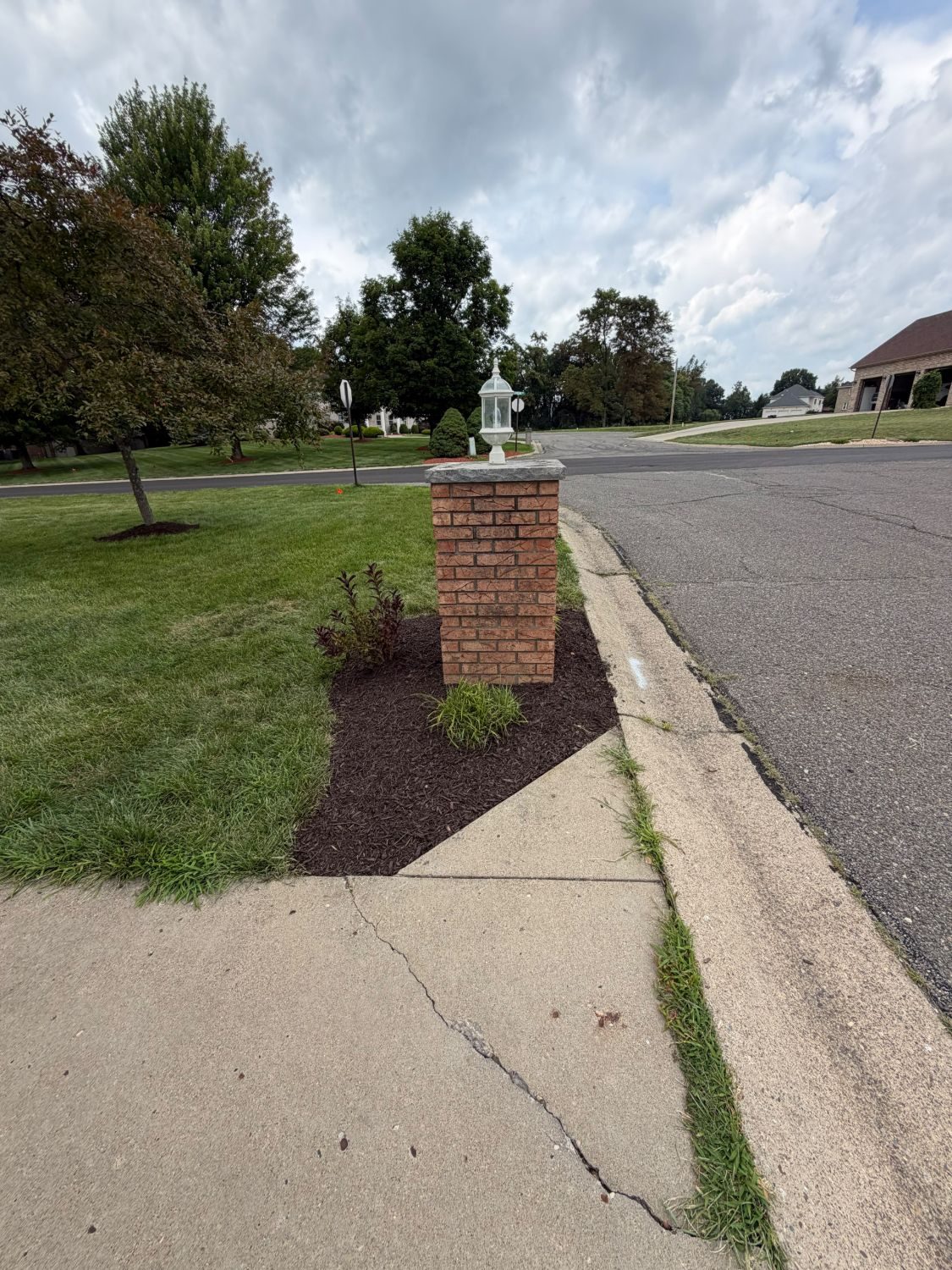 Brick mailbox pillar with fresh mulch bed and ornamental grass planting